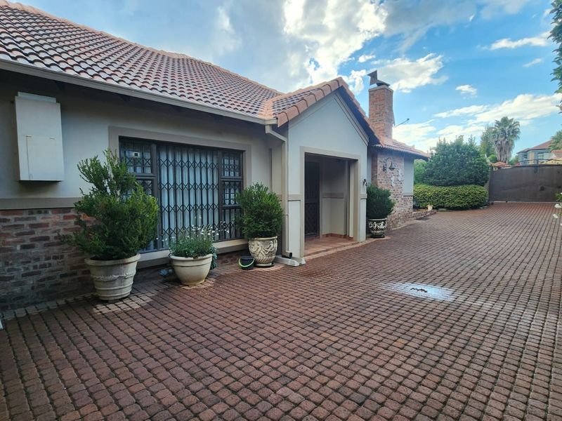 Front exterior view of a single-story house featuring a tiled roof, brick accents, and a spacious paved driveway.