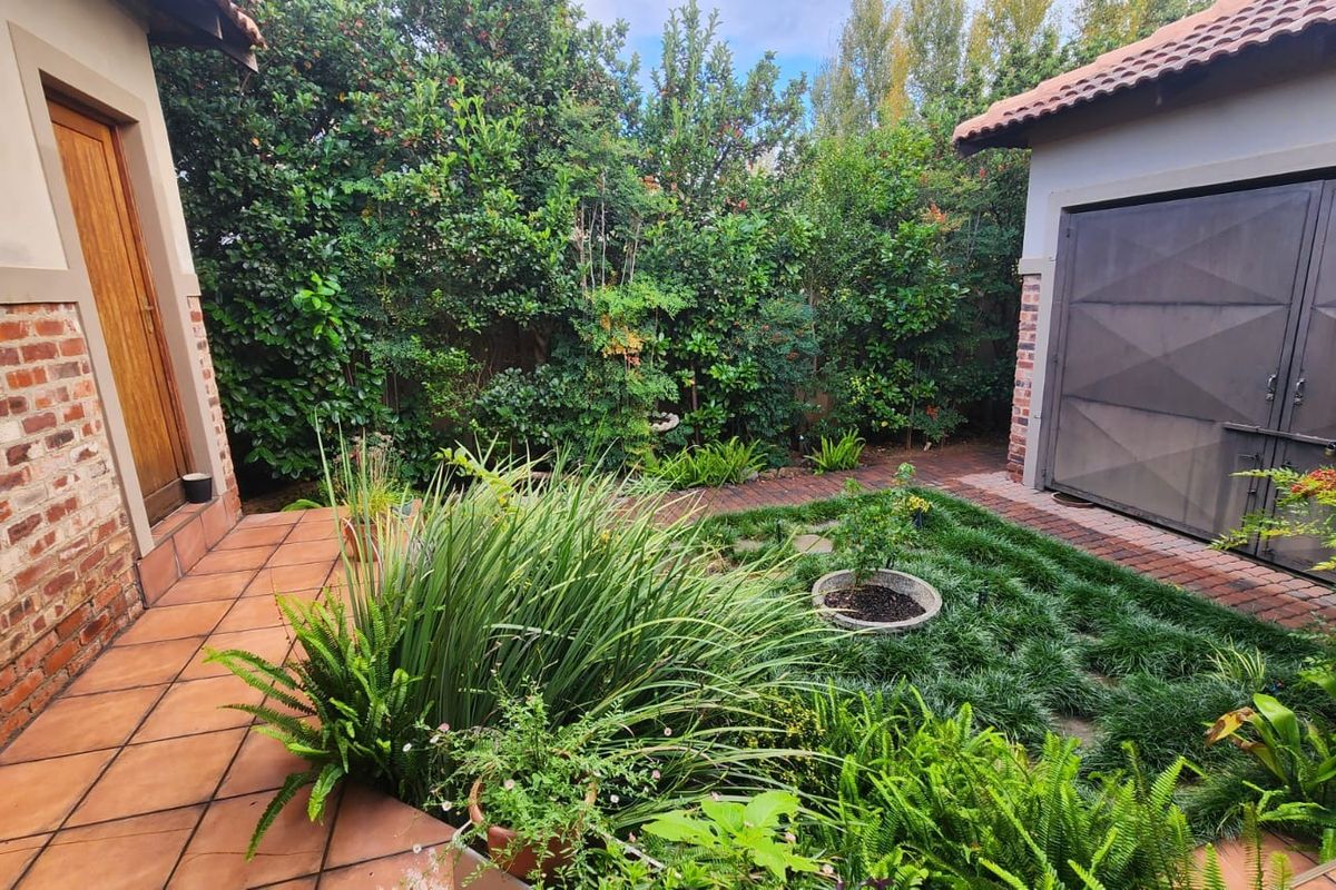 A well-maintained rear garden featuring a tiled patio, brick exterior walls, and a paved path leading to a garage.