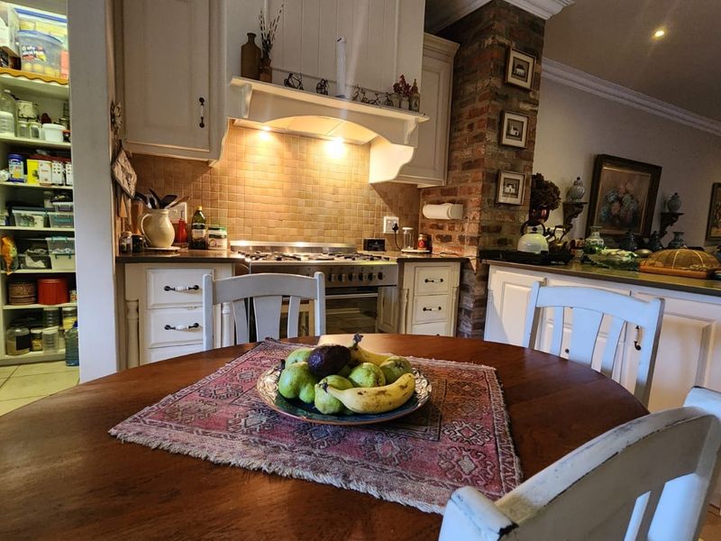 Open plan kitchen and dining area featuring classic white cabinetry, a gas stove with extractor, and a distinctive exposed brick feature pillar.