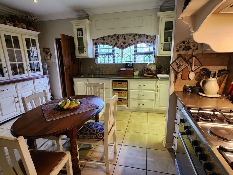 A traditional kitchen featuring white cabinetry, tiled countertops, a gas hob with oven, and a dedicated dining area with a built-in display cabinet.