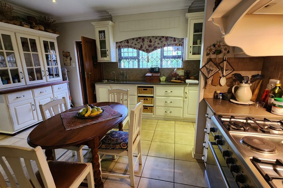 A traditional kitchen featuring white cabinetry, tiled countertops, a gas hob with oven, and a dedicated dining area with a built-in display cabinet.