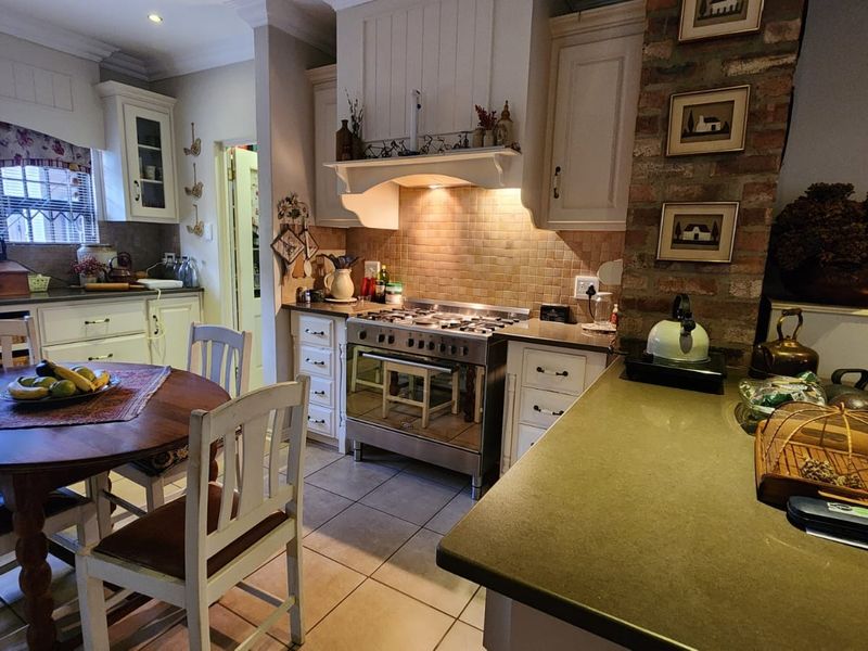 A charming kitchen featuring a gas stove, extractor fan, tiled backsplash, and an exposed brick feature wall with ample built-in cabinetry.