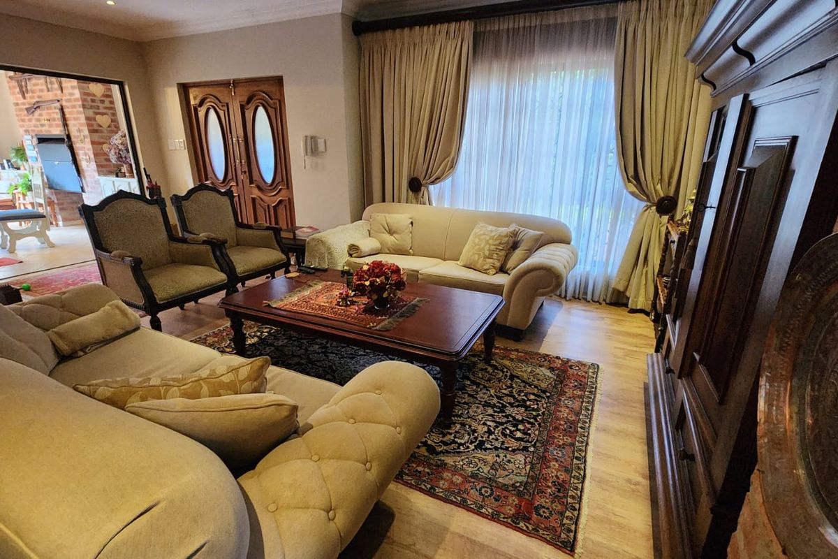 A spacious living room featuring laminate flooring, coved cornicing, and double wooden entrance doors, with direct access to an adjoining covered patio area.
