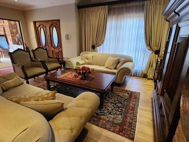 A spacious living room featuring laminate flooring, coved cornicing, and double wooden entrance doors, with direct access to an adjoining covered patio area.