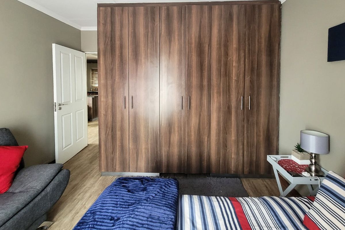 A bedroom featuring dark wood-finish built-in cupboards and laminate flooring, with an open doorway leading to an adjacent living space.