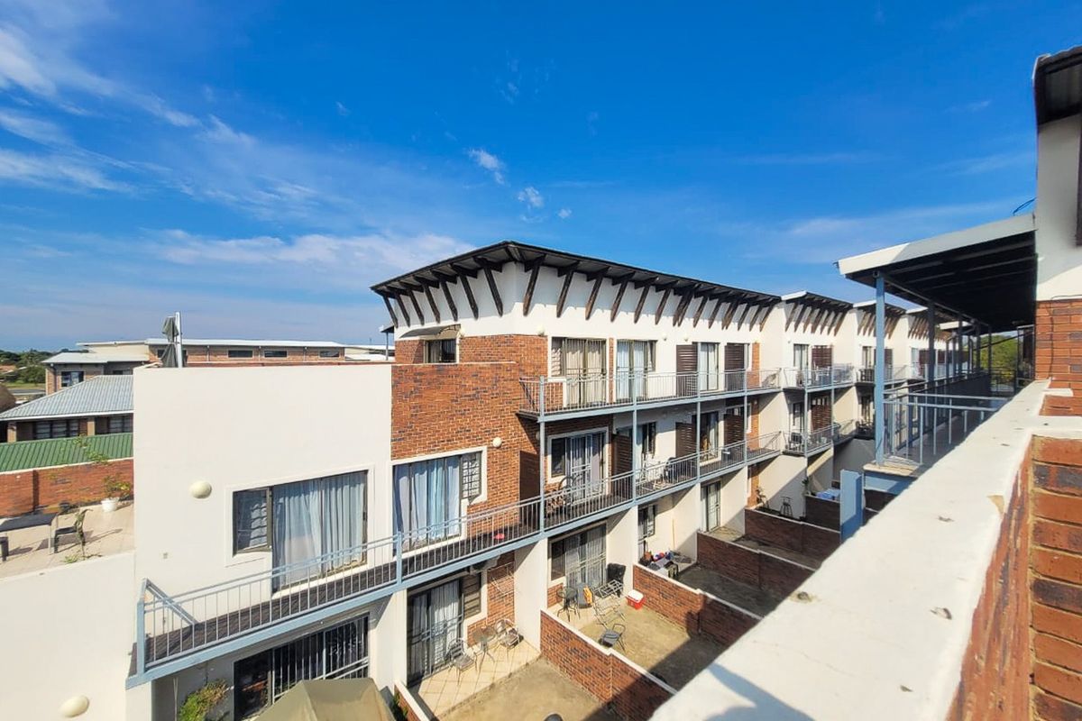 Exterior view of a multi-story apartment complex featuring brick and plaster facades, private balconies, and ground-level paved courtyards.