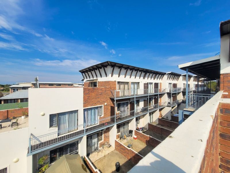 Exterior view of a multi-story apartment complex featuring brick and plaster facades, private balconies, and ground-level paved courtyards.