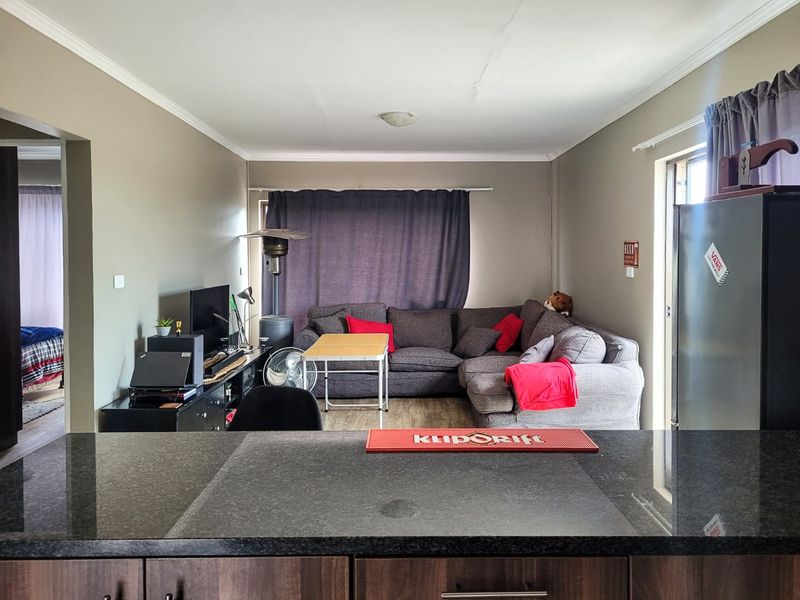 Open-plan living area featuring a dark granite kitchen breakfast bar, laminate flooring, and neutral wall tones, providing a functional and connected living space.