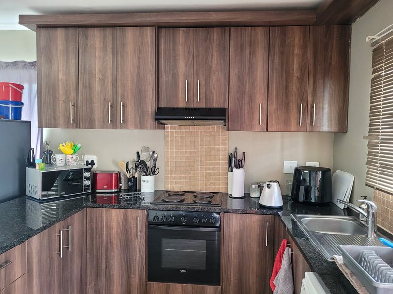 A functional kitchen featuring dark wood-look cabinetry, granite countertops, a built-in oven with electric hob, and a tiled splashback.