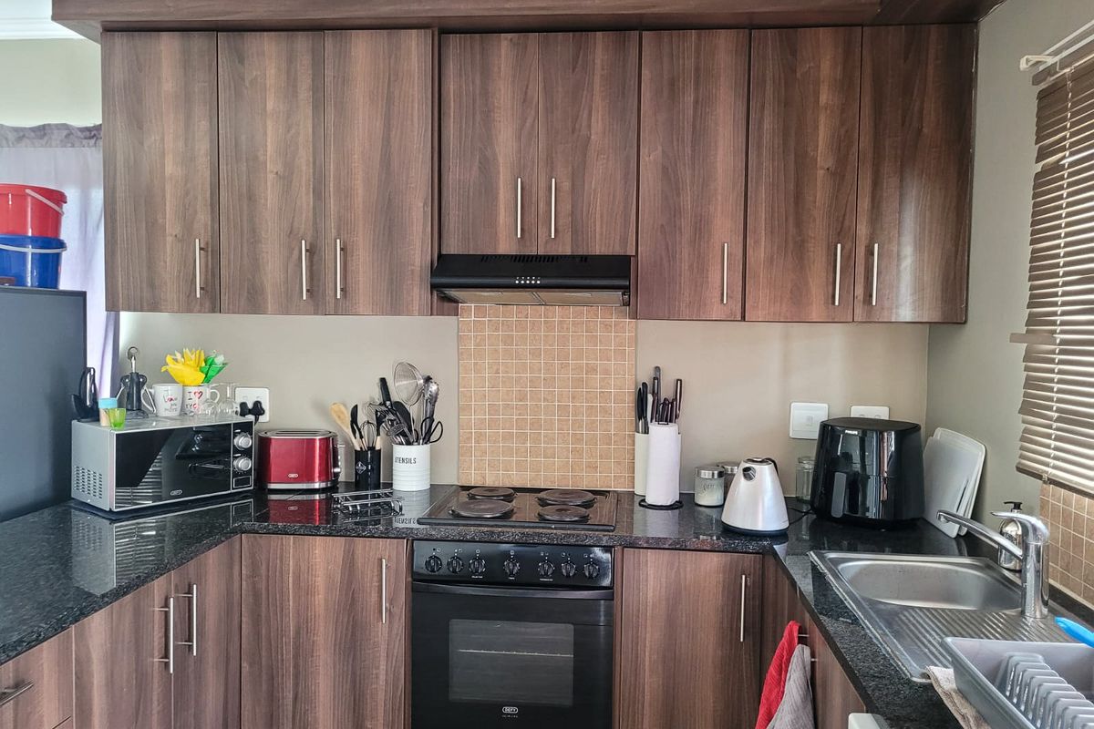 A functional kitchen featuring dark wood-look cabinetry, granite countertops, a built-in oven with electric hob, and a tiled splashback.
