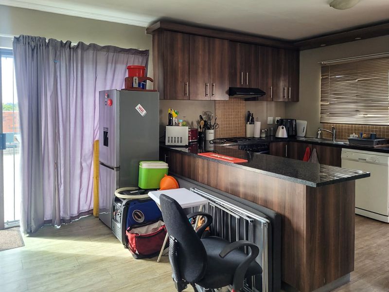 Open-plan kitchen featuring dark wood cabinetry, granite countertops, and integrated appliances, flowing into a living area with access to a balcony.