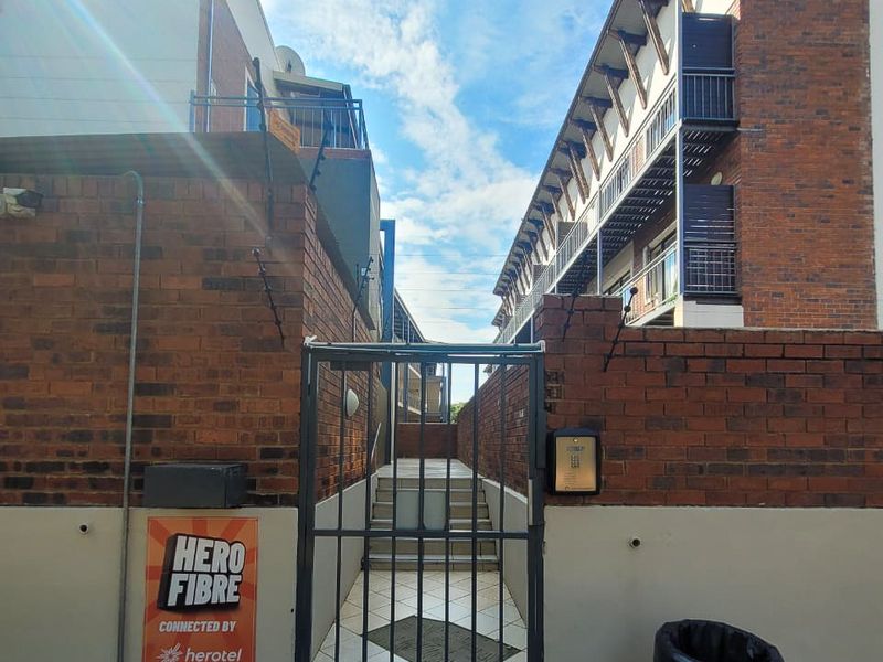 Exterior view of an apartment complex entrance featuring a secure metal gate, brick facade, and intercom system.