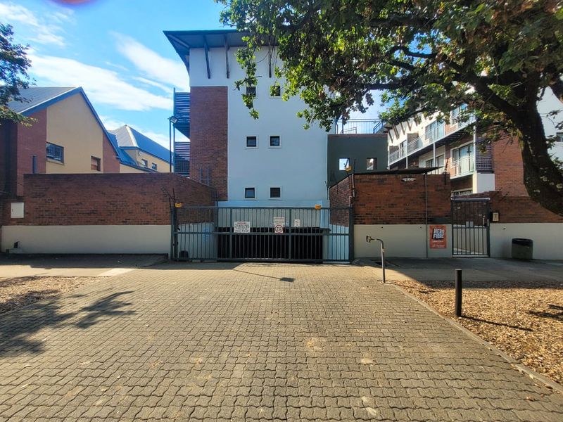 Exterior view of the apartment complex entrance featuring a paved driveway, secure gated access, and brick boundary walls with electric fencing.