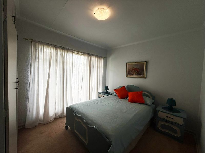 A functional bedroom featuring built-in cupboards and large windows with curtains, providing a comfortable and well-lit space.
