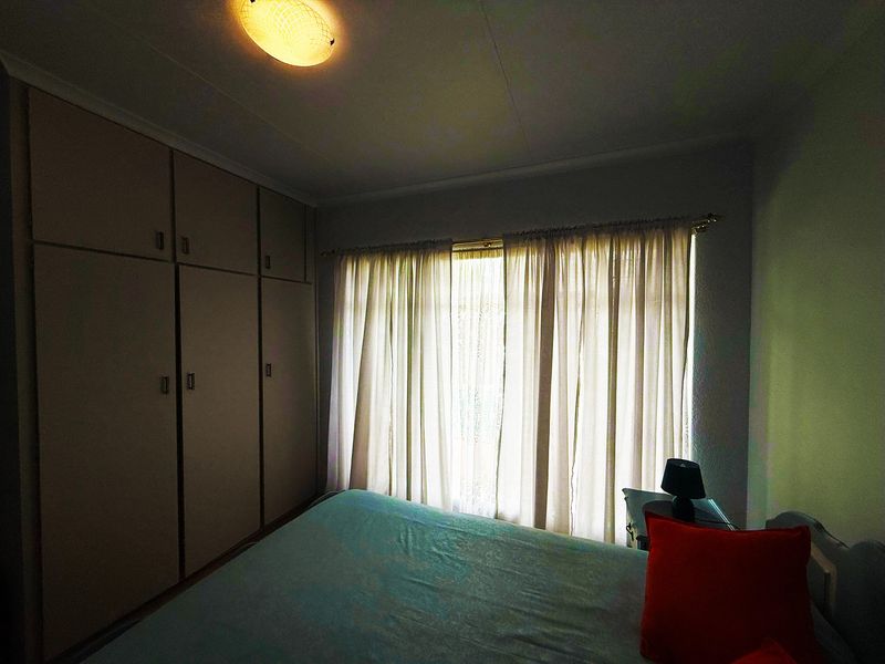 A bedroom featuring built-in cupboards and a window with curtains, providing functional storage and natural light.