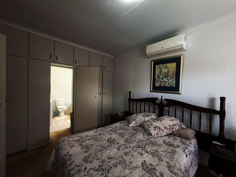 A bedroom featuring built-in cupboards, a wall-mounted air conditioning unit, and direct access to an en-suite bathroom.
