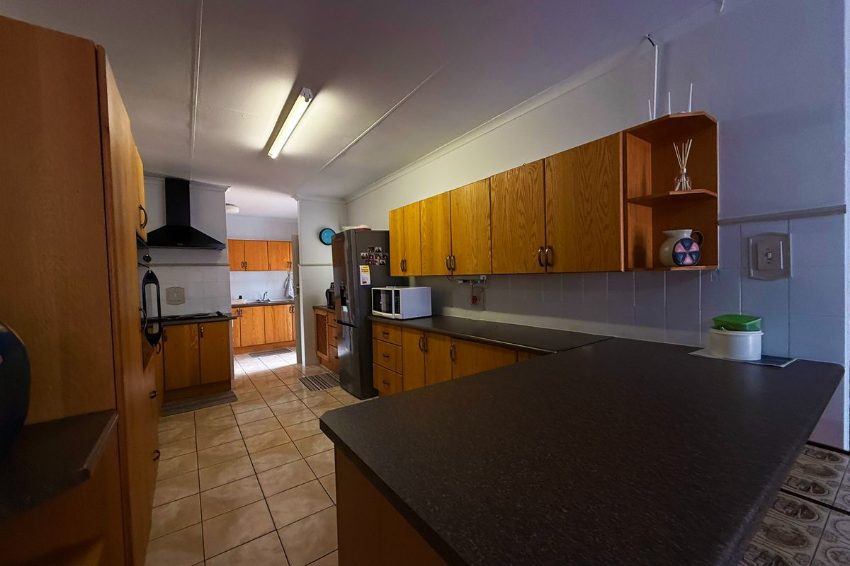 A functional kitchen featuring wood-look laminate cabinetry, dark countertops, tiled flooring, and a built-in extractor fan, offering a classic layout with ample storage space.