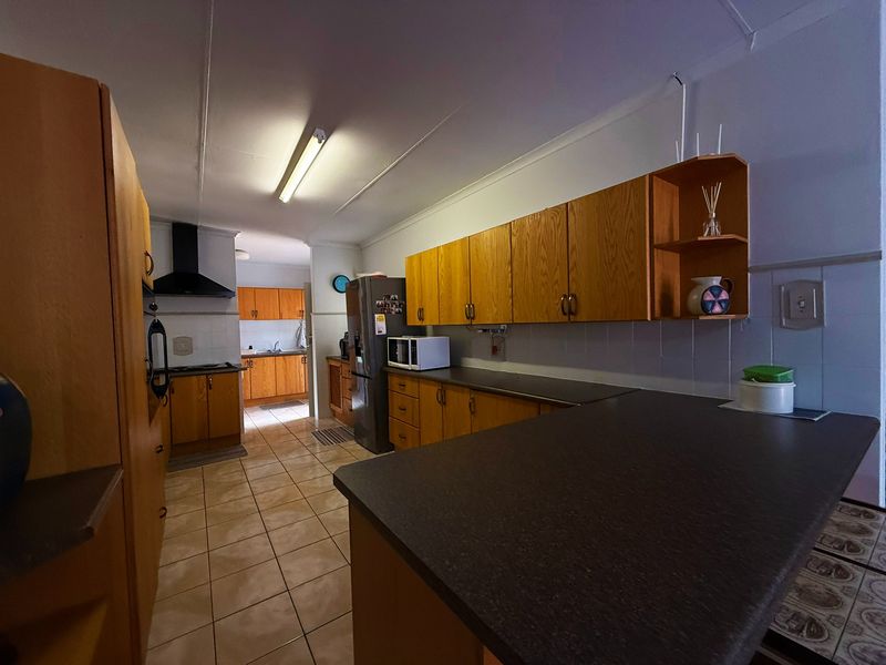 A functional kitchen featuring wood-look laminate cabinetry, dark countertops, tiled flooring, and a built-in extractor fan, offering a classic layout with ample storage space.