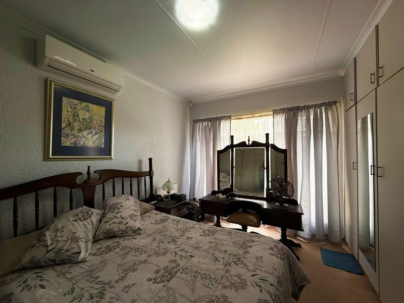 A functional bedroom featuring built-in storage cupboards, a wall-mounted split-system air conditioner, and carpeted flooring.