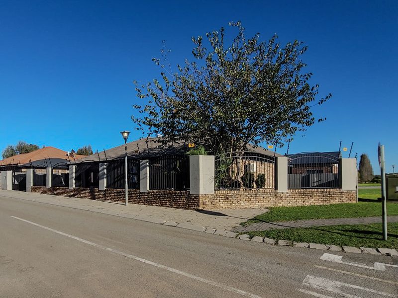 Street view of the property featuring a secure brick boundary wall with metal and electric fencing, tiled roof, and paved sidewalk.