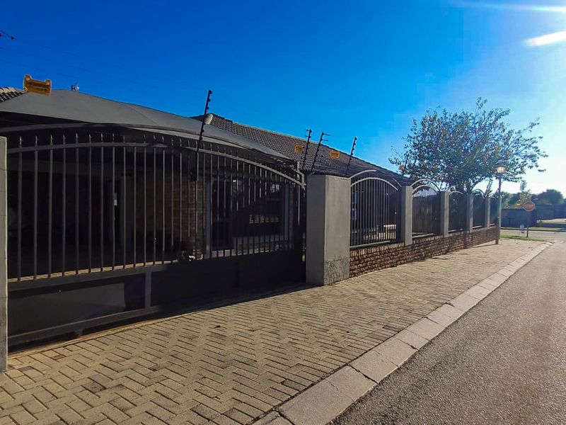 Front exterior view of the property featuring a secure metal gate, brick boundary wall with electric fencing, and a paved driveway.
