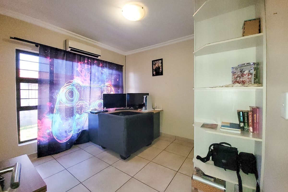 A functional bedroom featuring tiled flooring, a built-in shelving unit, and an air conditioning unit, currently utilized as a home office space.