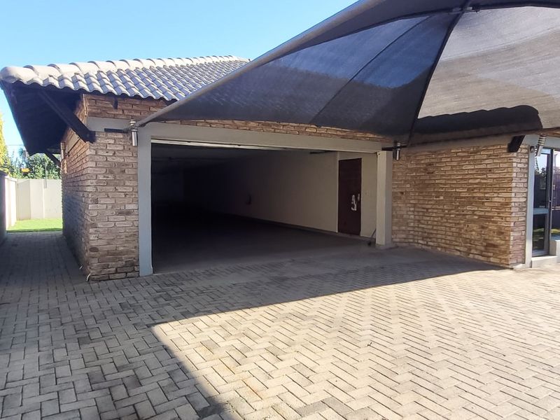 A spacious garage featuring a brick exterior, tiled roof, and a paved driveway with an overhead shade sail for vehicle protection.