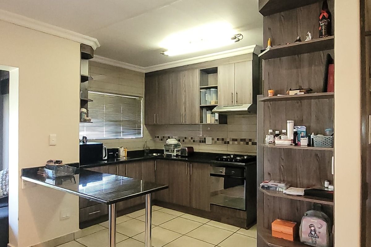 A functional kitchen featuring dark wood cabinetry, granite countertops, a breakfast bar, and integrated appliances, complemented by tiled flooring and built-in shelving.