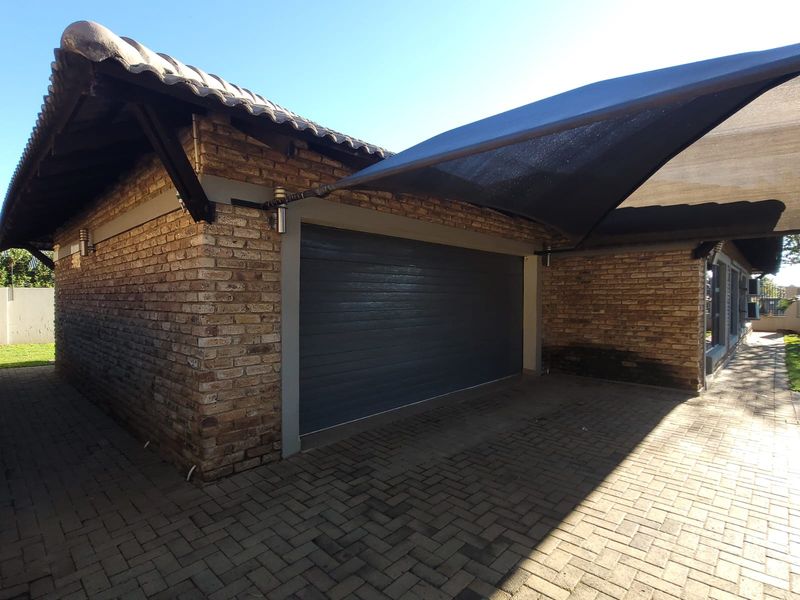 A well-maintained brick garage featuring a modern sectional door and an attached shade sail over the paved driveway area.