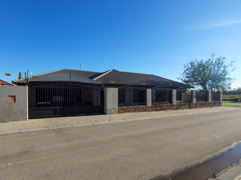 Front exterior view of a single-story house featuring a tiled roof, brick facade, and secure perimeter wall with metal gates and electric fencing.
