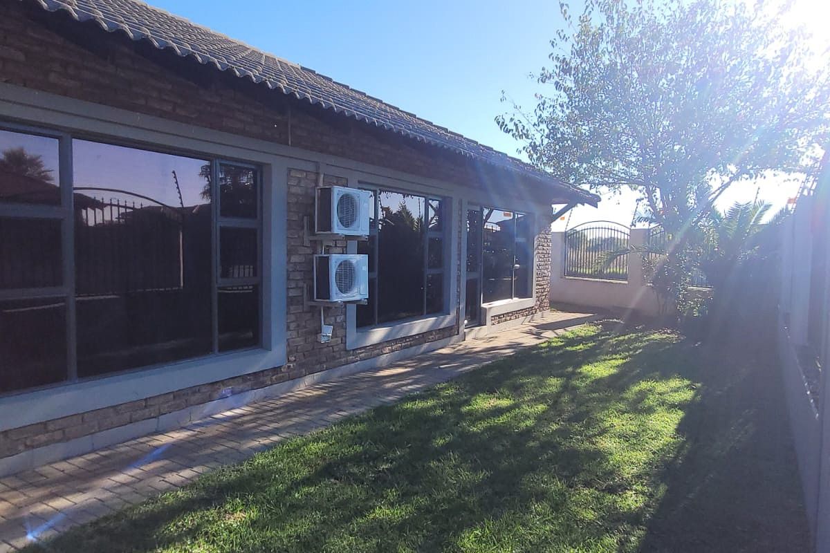 Rear view of the property featuring a brick facade, paved walkway, well-maintained lawn, and installed air conditioning units.
