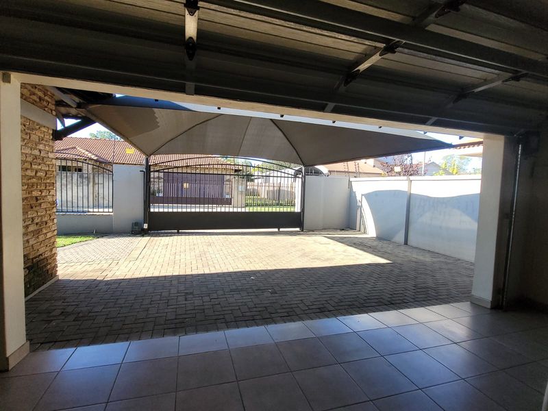 A paved driveway area featuring a shade sail, enclosed by a perimeter wall and a secure metal gate, viewed from the garage entrance.