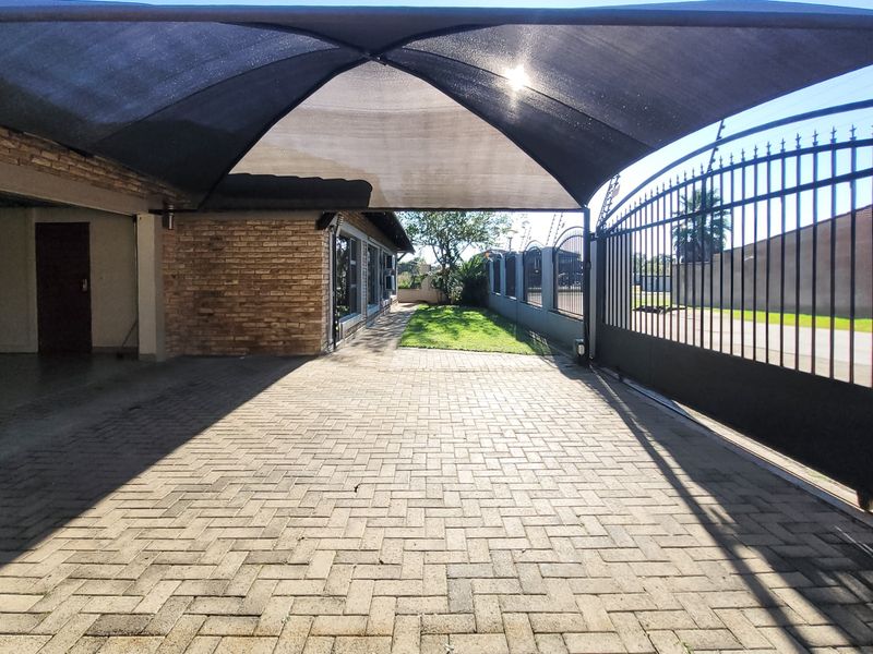 Front exterior view featuring a paved driveway, secure wrought iron gate, and a protective shade sail structure over the parking area.