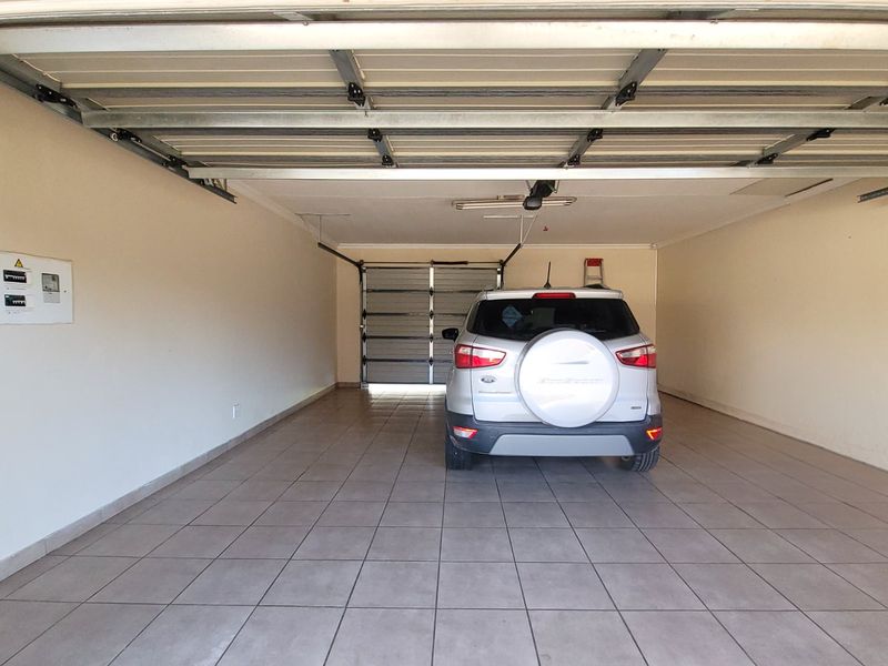 A spacious, well-maintained double garage featuring tiled flooring, a sectional overhead door, and a wall-mounted electrical distribution board.