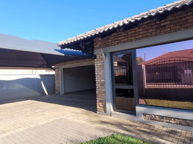 Front exterior view featuring a brick facade, tiled roof, paved driveway, and a covered carport area with a glass entrance door.