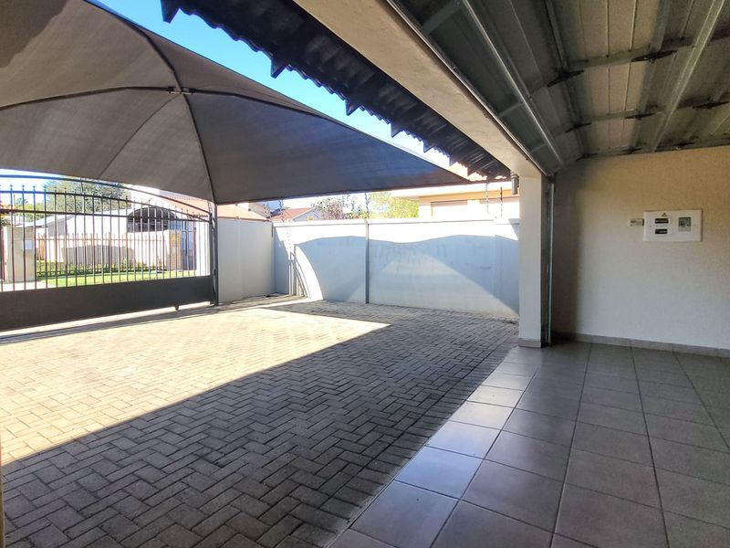 A spacious paved garage area featuring a shade sail, secure perimeter walling, and a metal gate, providing ample covered parking space.