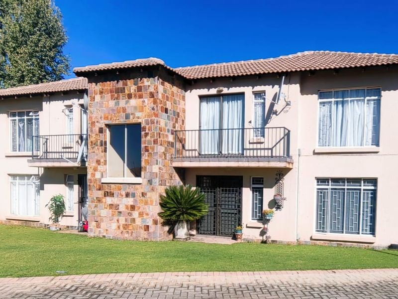 Front elevation of a two-story apartment building featuring stone cladding accents, tiled roofing, balconies with metal railings, and a well-maintained lawn.