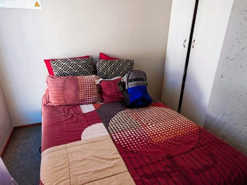 A compact bedroom featuring a built-in wardrobe, carpeted flooring, and textured wall finishes, offering a functional space for rest.