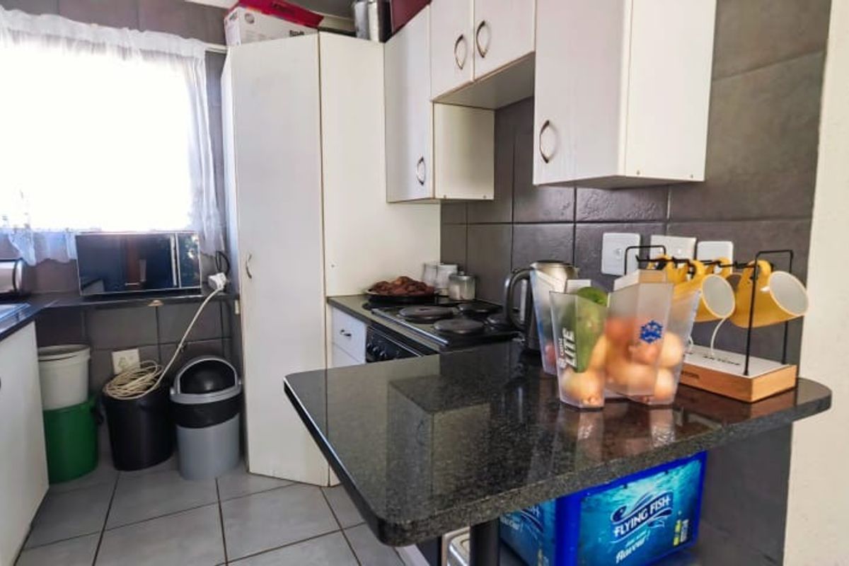 Compact kitchen featuring granite countertops, built-in white cabinetry, electric hob, and dark tiled backsplash, offering a functional layout for apartment living.