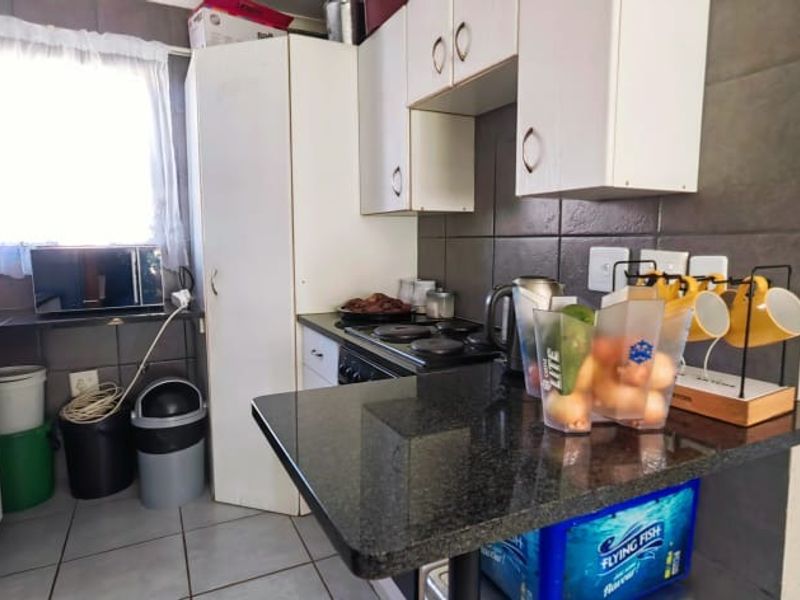 Compact kitchen featuring granite countertops, built-in white cabinetry, electric hob, and dark tiled backsplash, offering a functional layout for apartment living.