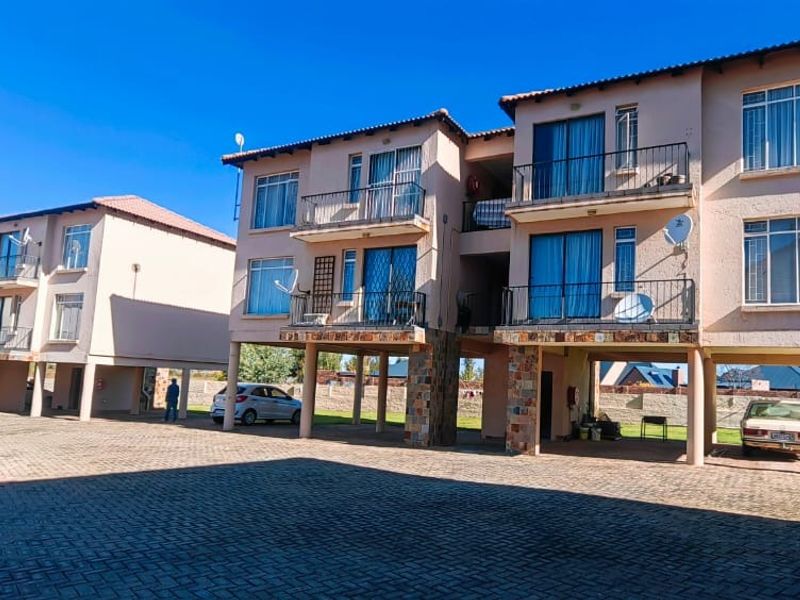 Exterior view of a multi-story apartment complex featuring stilted construction, paved parking areas, and private balconies for each unit.