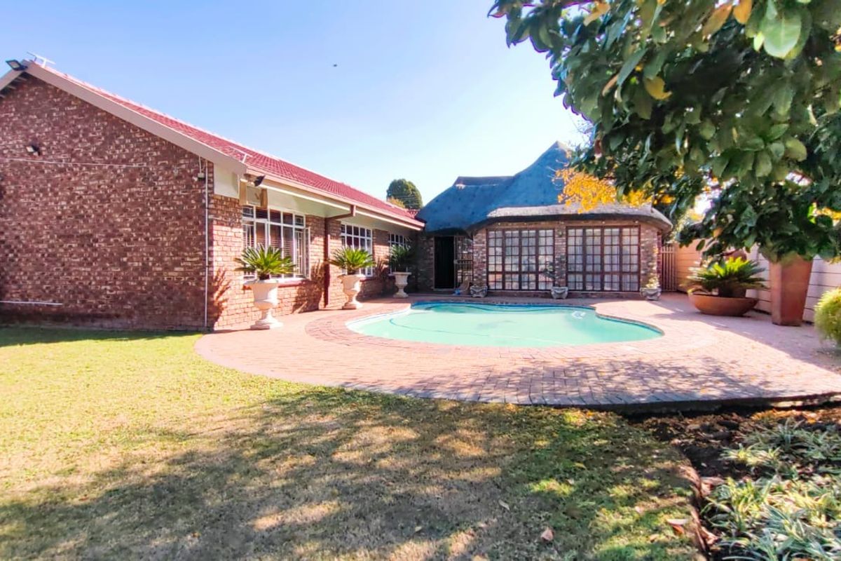 A spacious rear garden featuring a swimming pool, brick-paved patio area, and a combination of face brick and thatched roof architecture.