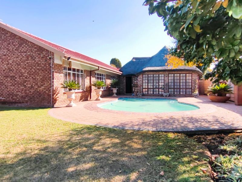 A spacious rear garden featuring a swimming pool, brick-paved patio area, and a combination of face brick and thatched roof architecture.