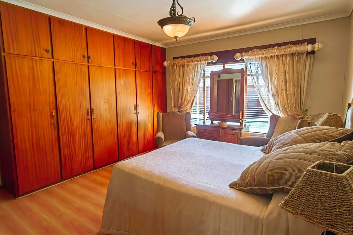 A spacious bedroom featuring extensive built-in wooden cabinetry, laminate flooring, and natural light through a window.