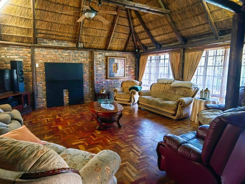 Spacious living room featuring a traditional thatched roof, exposed brick walls, and classic parquet flooring, creating a warm and rustic atmosphere.