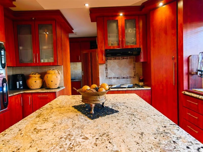 A spacious kitchen featuring extensive wooden cabinetry, granite countertops, a central island, and built-in appliances including an oven and hob.