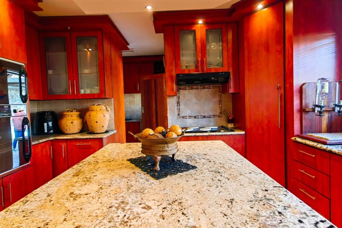 A spacious kitchen featuring extensive wooden cabinetry, granite countertops, a central island, and built-in appliances including an oven and hob.