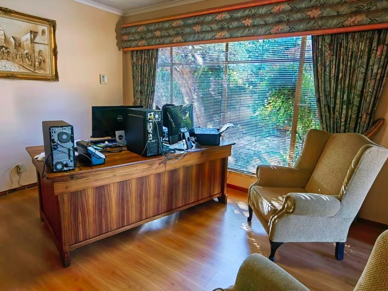 A functional home office space featuring laminate flooring, large windows with venetian blinds, and classic cornicing, providing a quiet area for work or study.