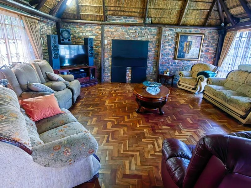 Spacious living room featuring rustic exposed brick walls, traditional thatched roofing with exposed timber beams, and classic parquet flooring.