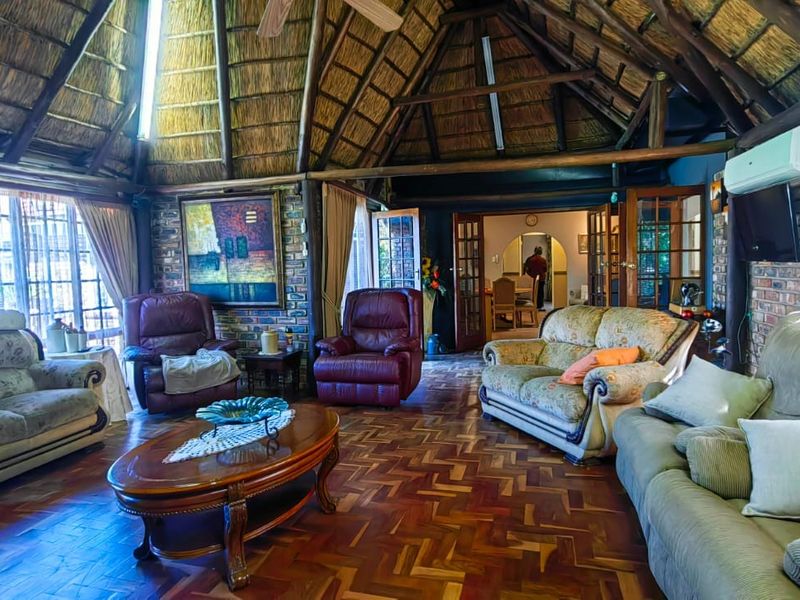 Spacious living room featuring a high vaulted thatched ceiling with exposed timber beams, parquet flooring, and exposed brick walls.